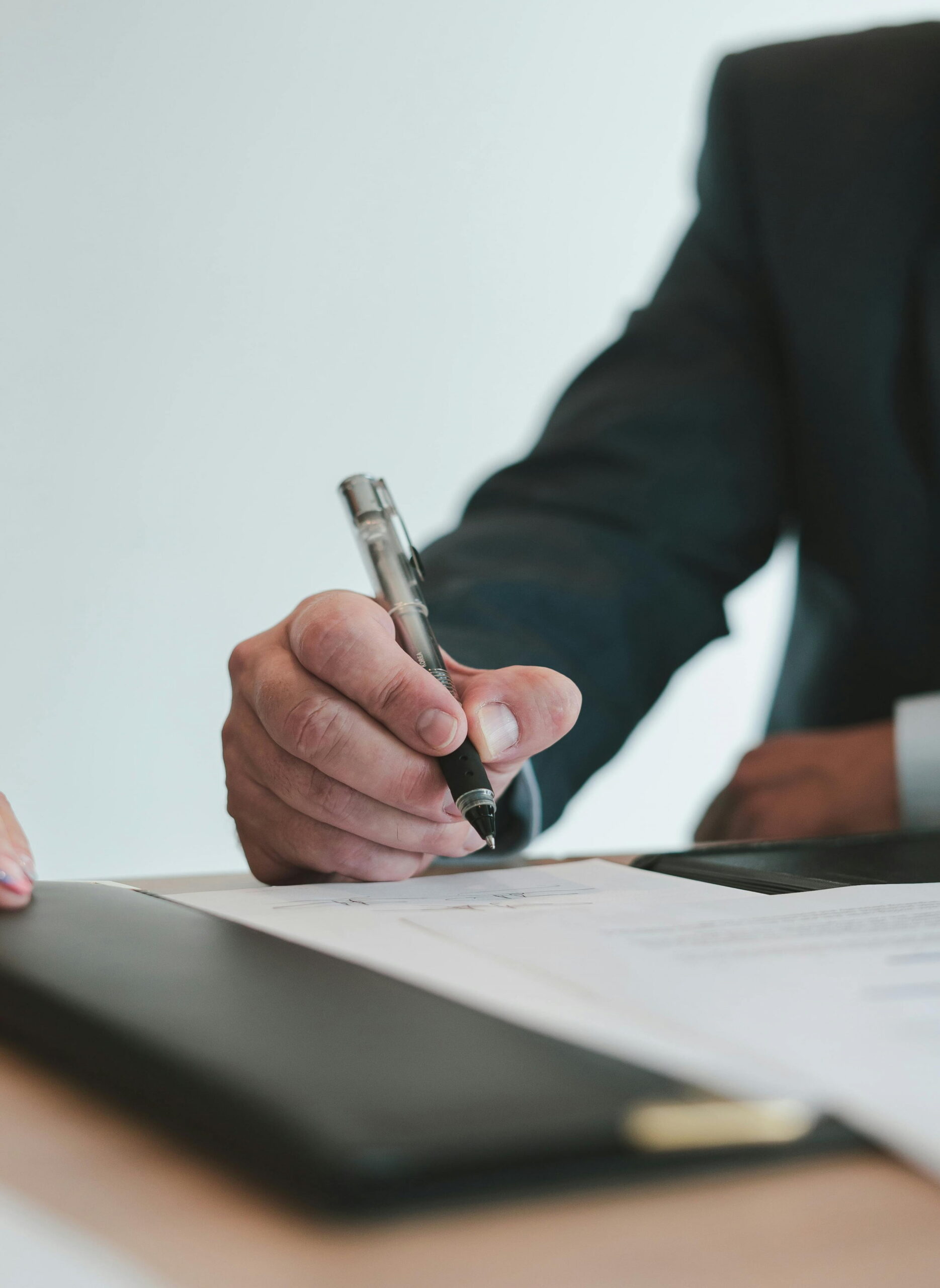Close-up of a businessman in a suit signing a document or contract with a black pen.