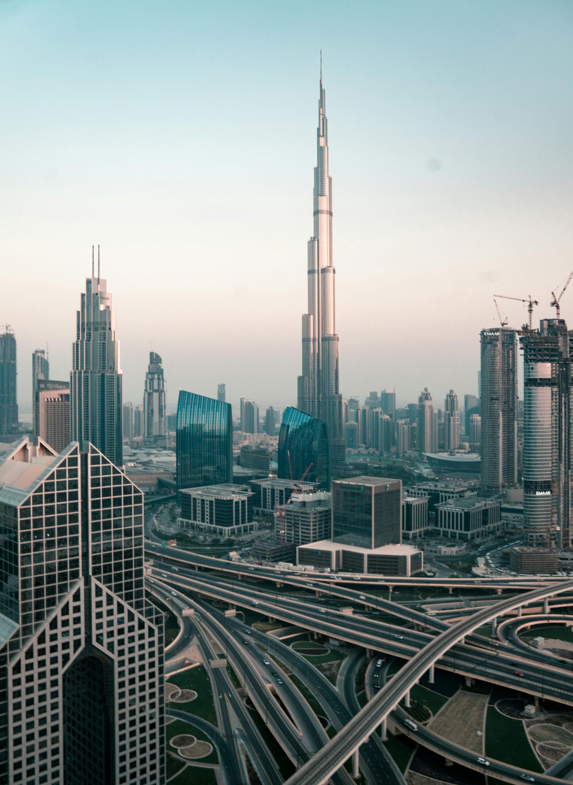 View of the Dubai skyline at dawn featuring Burj Khalifa surrounded by skyscrapers and highway interchanges.